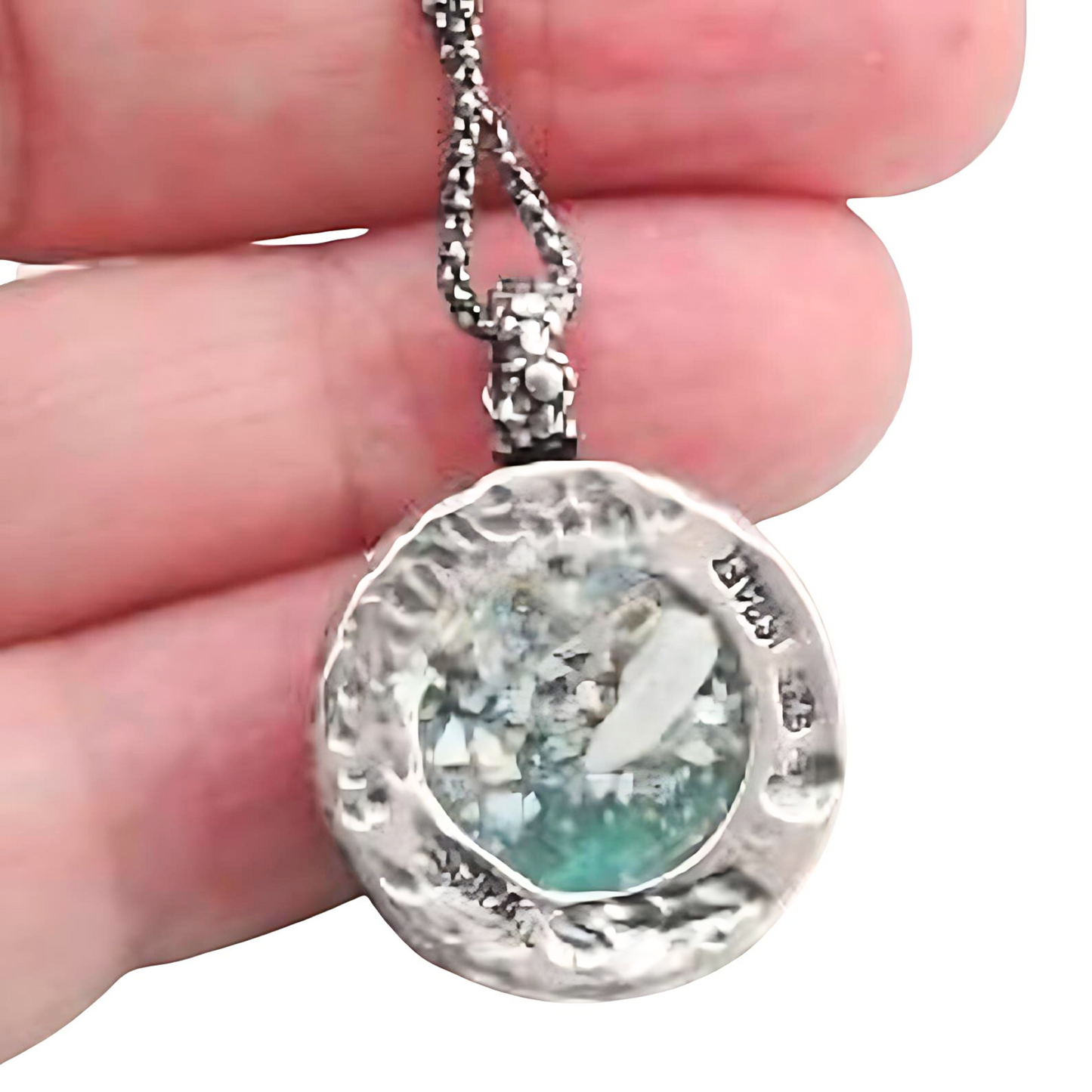 Handcrafted sterling silver pendant featuring a round Roman glass centerpiece in shades of light blue and silver. The unique, textured chain complements the pendant, creating a distinctive, artisanal look. Shown held in hand to display its intricate details and delicate craftsmanship