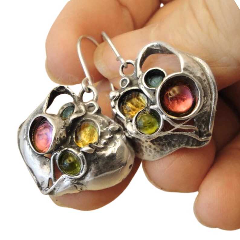 Close-up view of elegant, handcrafted heart-shaped silver earrings, featuring a unique, intricate design with multicolored glass beads in shades of emerald green, amber, and golden yellow. The earrings showcase a vintage-inspired aesthetic with a delicate arrangement of glass stones, adding a touch of sophistication and artistic charm